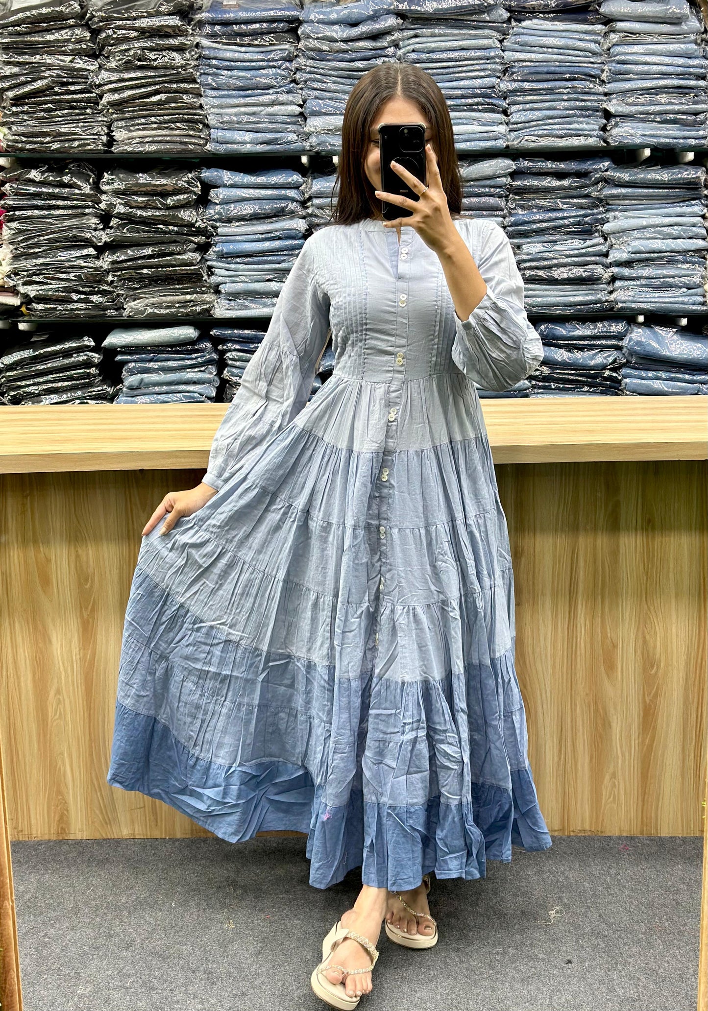 Woman wearing blue gradient ethnic cotton frock online style posing in front of stacked fabric at Vinayak Fashion