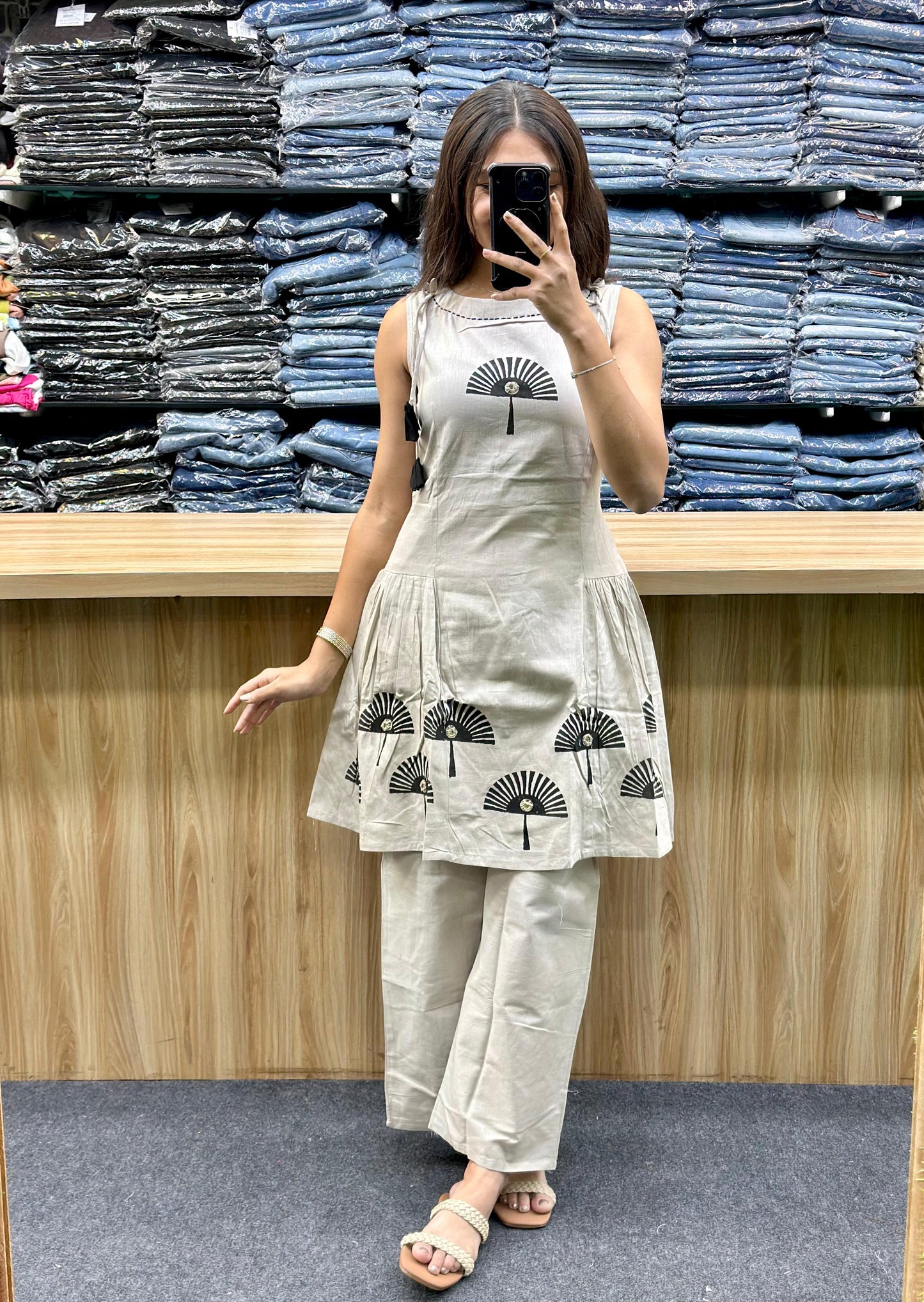 Woman wearing latest designer co-ord set in beige with black fan print posing in front of denim shelves