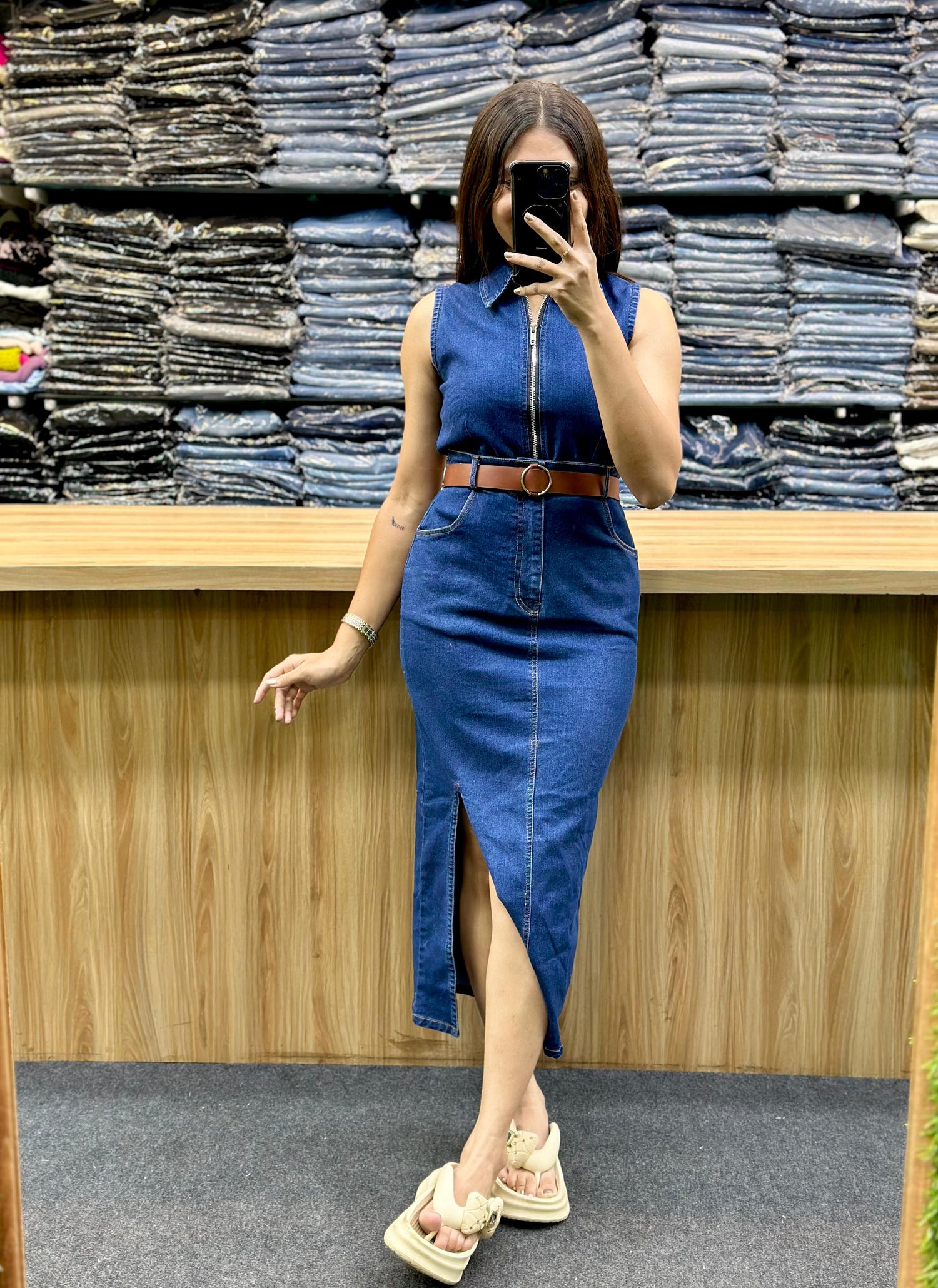 Woman modeling casual outfit with printed blouse and olive green pants in front of stacked denim jeans collection
