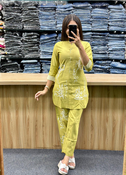 Woman wearing yellow cotton loungewear set with white floral designs standing in front of folded denim stacks