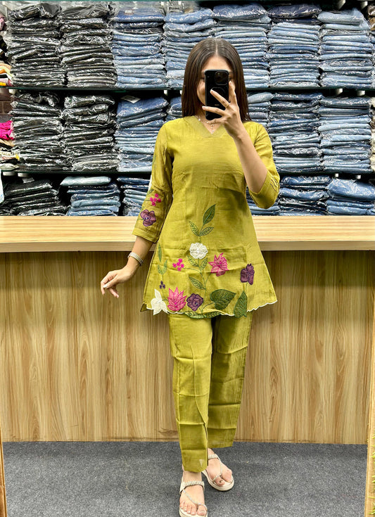Green embroidered cotton kurti with pants featuring colorful floral designs worn by a woman in a clothing store