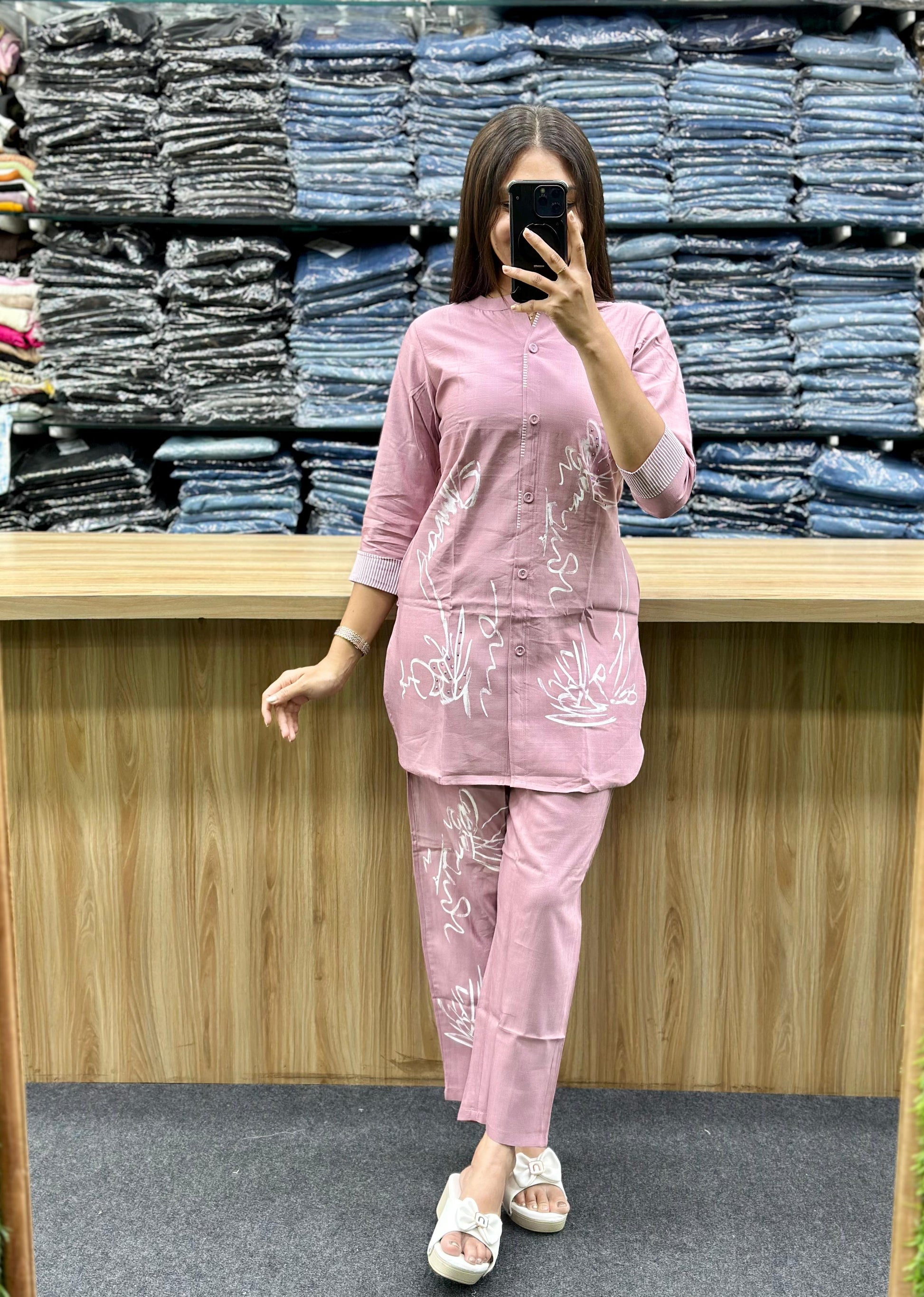 Woman wearing a pink cotton loungewear set with white floral prints standing in front of folded jeans