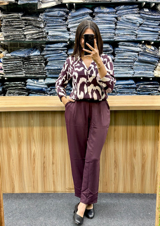 Woman wearing maroon printed top and maroon pants standing in front of stacked denim jeans at Vinayak Fashion
